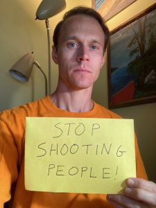 Kenneth holding a sign that says "Stop Shooting People!"