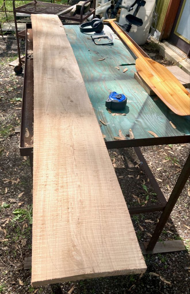 A rough cut board sitting on a table, next to some tools and an older otter tail paddle