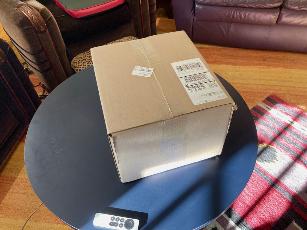 a cardboard shipping box sitting on a coffee table.  An Apple TV remote rests in the foreground.