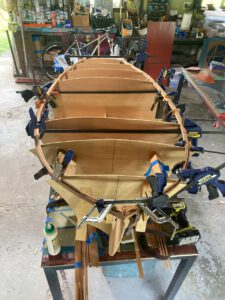 Wooden boat under construction. Clamps holding in place strips making up the rails of the boat.