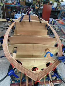 Wooden boat under construction. Clamps holding in place strips making up the rails of the boat.