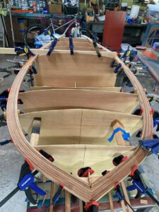 Wooden boat under construction. Clamps holding in place strips making up the rails of the boat.