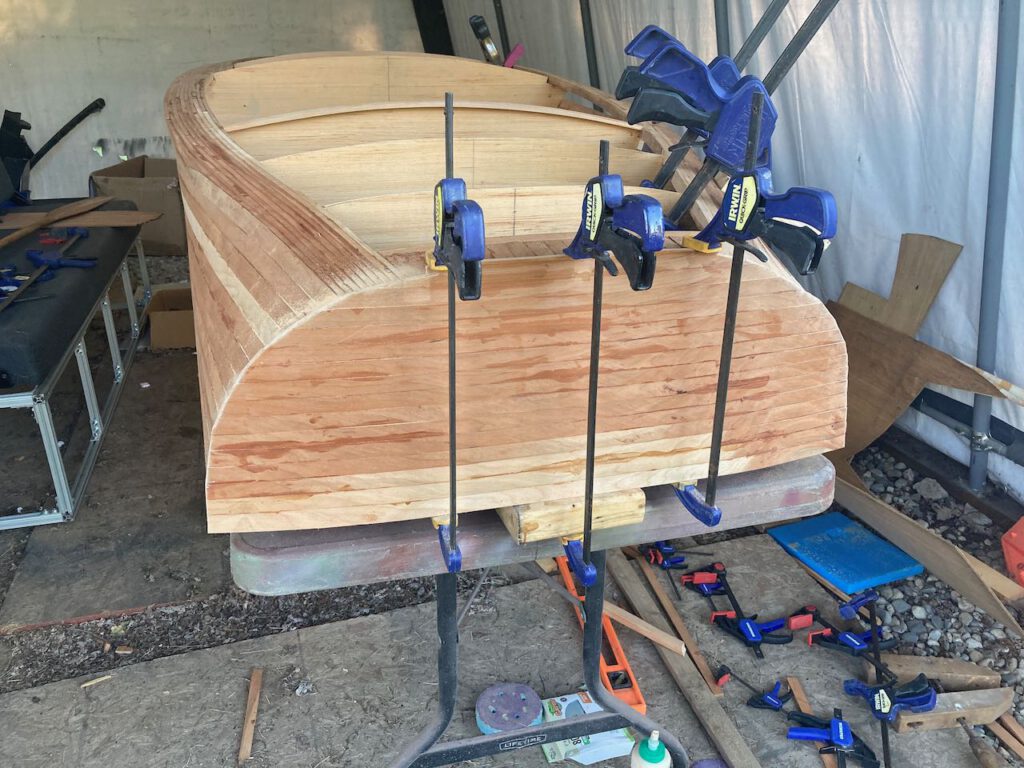 Wooden boat under construction. Clamps holding in place the final strip of cherry on the aft of the vessel.