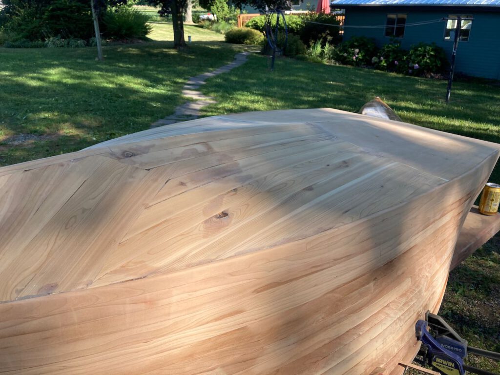 Wooden boat under construction, upside down on a table. The hull is roughly sanded.