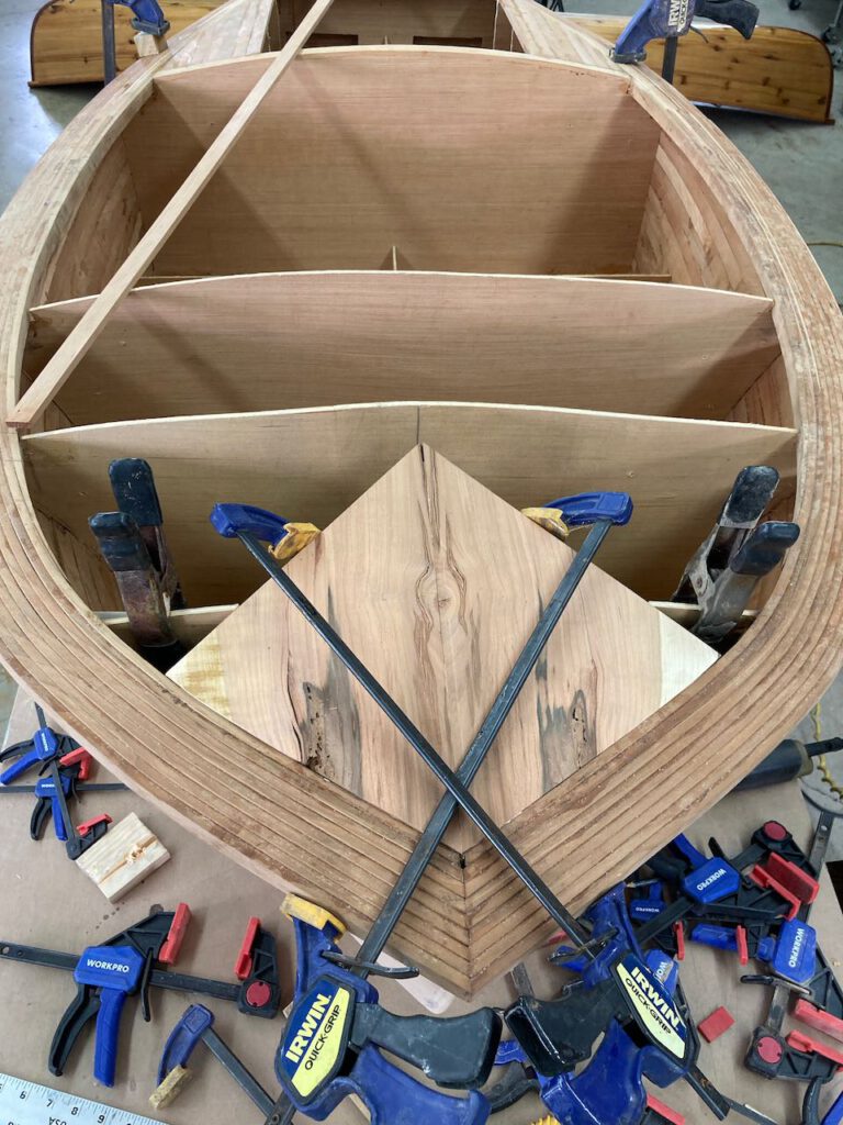 Wooden boat under construction. A carefully selected and bookmatched cherry inlay is clamped into the bow of the boat.