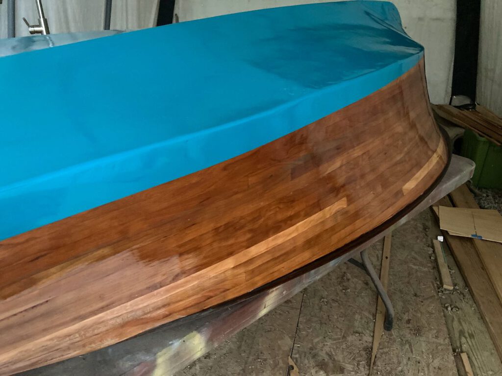 A wooden boat, upside down, with two coats of varnish on the hull.