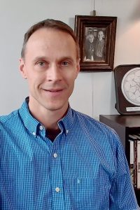 Kenneth sitting at his desk, with a bookshelf and hanging artwork behind him